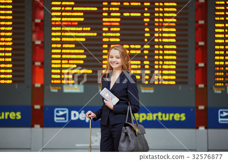 Young woman in international airport looking at the flight information board, checking her flight 32576877