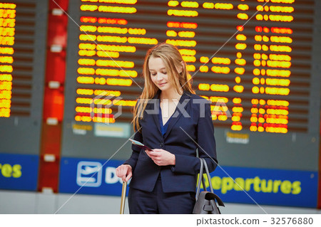 Woman with hand luggage in international airport terminal, looking at information board 32576880