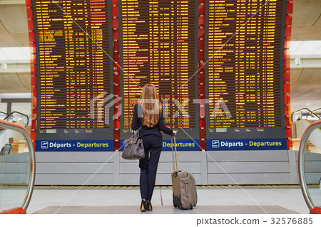 Woman with hand luggage in international airport terminal, looking at information board 32576885