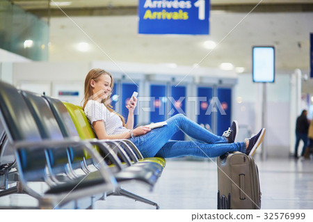 Young travelerin international airport checking her mobile phone while waiting for her flight 32576999