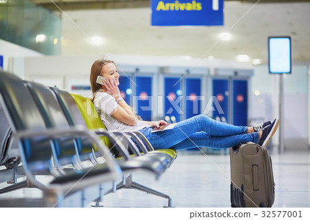Young travelerin international airport checking her mobile phone while waiting for her flight Young travelerin international airport checking her mobile phone while waiting for her flight 32577001