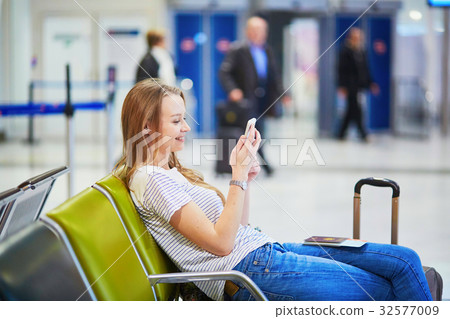 Young travelerin international airport checking her mobile phone while waiting for her flight Young travelerin international airport checking her mobile phone while waiting for her flight 32577009