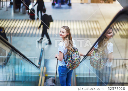 Tourist girl with backpack and carry on luggage in international airport, on escalator 32577028