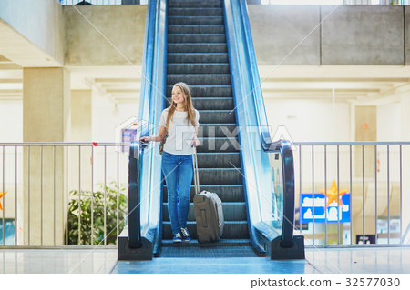 Tourist girl with backpack and carry on luggage in international airport, on escalator 32577030