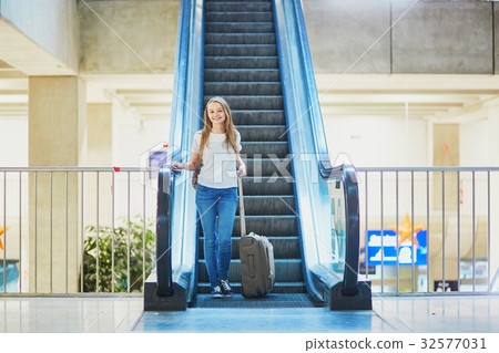 Tourist girl with backpack and carry on luggage in international airport, on escalator 32577031