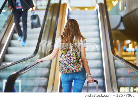 Tourist girl with backpack and carry on luggage in international airport, on escalator Tourist girl with backpack and carry on luggage in international airport, on escalator 32577065
