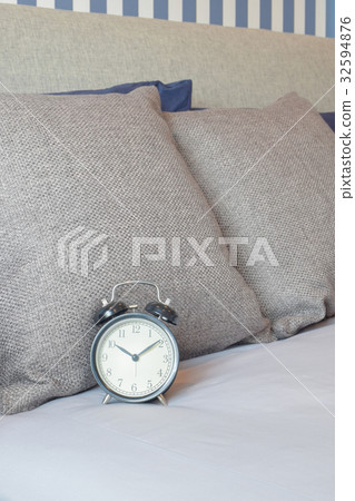Retro style clock setting on bed with brown pillow 32594876