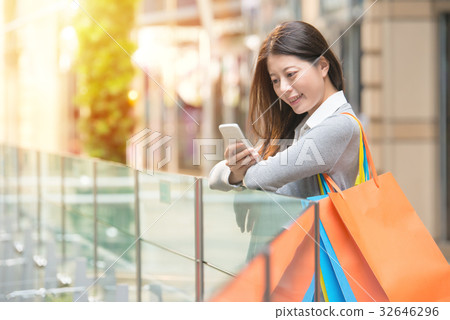 Happy girl holding with purchases looking at phone Happy girl holding with purchases looking at phone 32646296