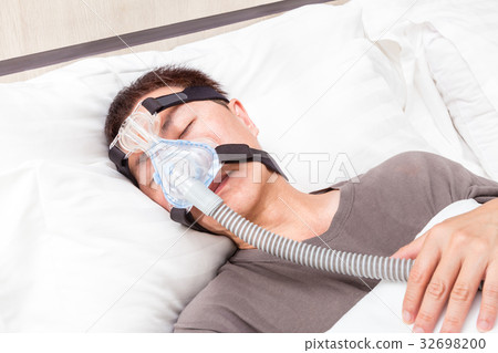 asian man sleeping wearing CPAP headgear 32698200