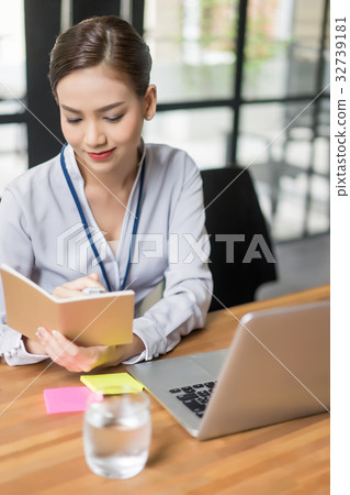The woman is sitting and reading the notebook. The woman is sitting and reading the notebook. 32739181