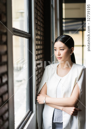 A woman is standing, looking through the window and thinking 32739195