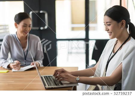 a business woman is typing on laptop and smiling next to a woman 32739237