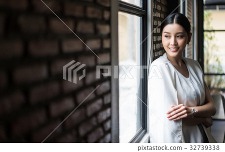 a smiling woman is leaning against a wall and looking at something a smiling woman is leaning against a wall and looking at something 32739338