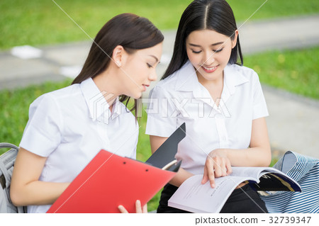 Two university students are looking at the book and smiling in the park Two university students are looking at the book and smiling in the park 32739347