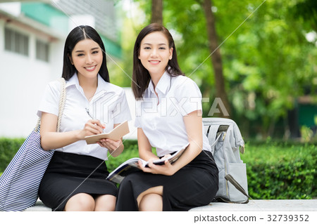 Two girls in uniform are smiling and sitting on the bench in the park 32739352
