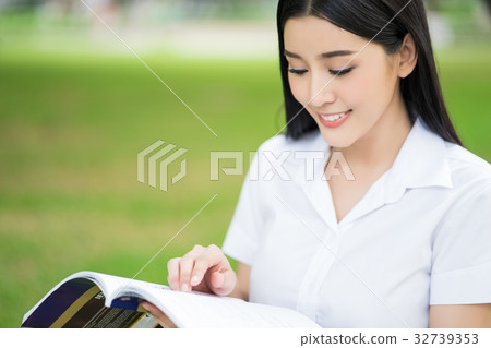 A female student is looking at the book and smiling in the park A female student is looking at the book and smiling in the park 32739353