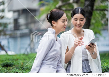 a picture of two women chatting and using the phone outdoors a picture of two women chatting and using the phone outdoors 32739483
