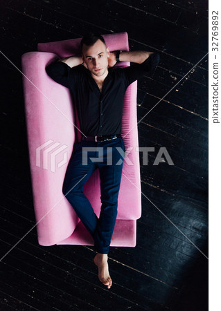 Man model sits on pink sofa in loft interior Man model sits on pink sofa in loft interior 32769892