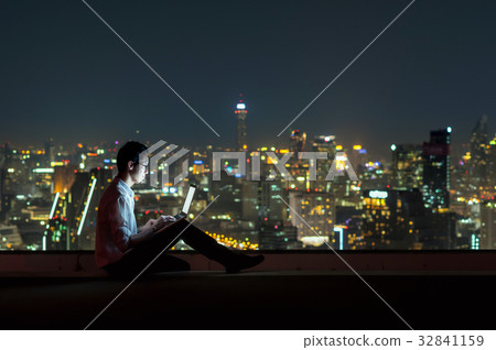 Asian businessman sitting and using the laptop over the cityscape background at night time, Business success and technology concept Asian businessman sitting and using the laptop over the cityscape background at night time, Business success and technology concept 32841159