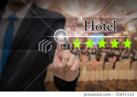 Businessman pointing five star button to increase rating of hotel over Abstract blurred photo of conference hall or seminar room with attendee background, business evaluation concept, Increase rating 32841310