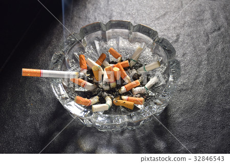 Lit cigarette with smoke lying on an ashtray 32846543
