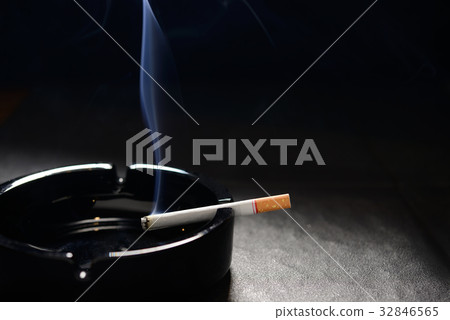 Lit cigarette with smoke lying on an empty ashtray Lit cigarette with smoke lying on an empty ashtray 32846565
