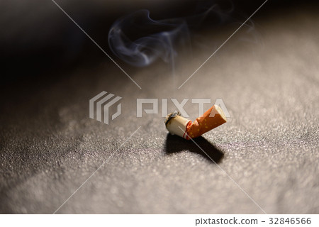 Lit cigarette butt with smoke on the ground Lit cigarette butt with smoke on the ground 32846566
