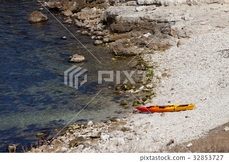 Orange kayak on pebbly beach of sea coast 32853727