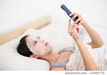 Woman using the facial mask and touch on the cellphone 32860770