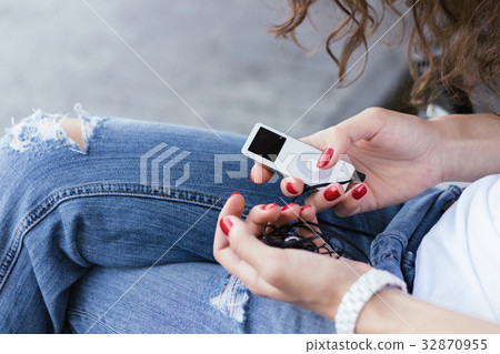 Girl in blue jeans holding a music player in hands Girl in blue jeans holding a music player in hands 32870955