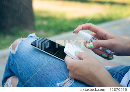 Woman in blue jeans cleans mobile phone Woman in blue jeans cleans mobile phone 32870956