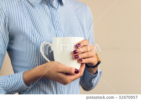 Woman in a blue striped shirt is holding a cup Woman in a blue striped shirt is holding a cup 32870957