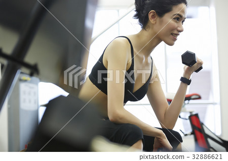 smiling woman is sitting and lifting dumbbell at sport club smiling woman is sitting and lifting dumbbell at sport club 32886621