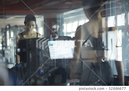 A girl is standing with modern machine and a mirror at fitness center 32886677