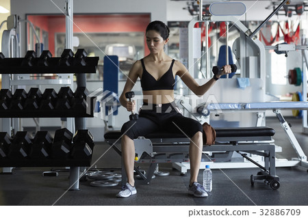 a woman is lifting a dumbbell by left hand and keeping one in the other a woman is lifting a dumbbell by left hand and keeping one in the other 32886709
