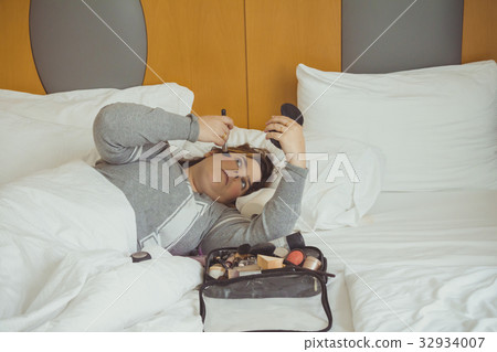 Woman applying makeup while she is lying on bed Woman applying makeup while she is lying on bed 32934007