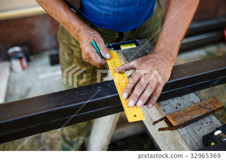 Man measuring off metal bar in workshop. 32965369