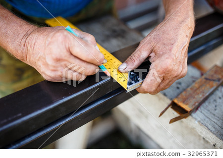 Man measuring off metal bar in workshop. 32965371