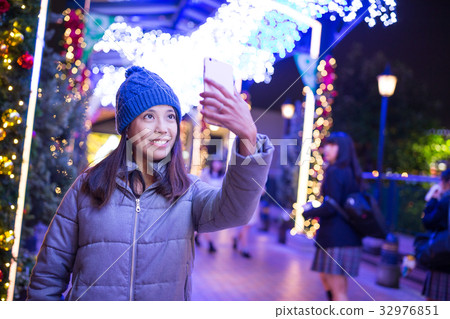 Woman taking selfie by mobile phone with christmas decoration at ngiht 32976851