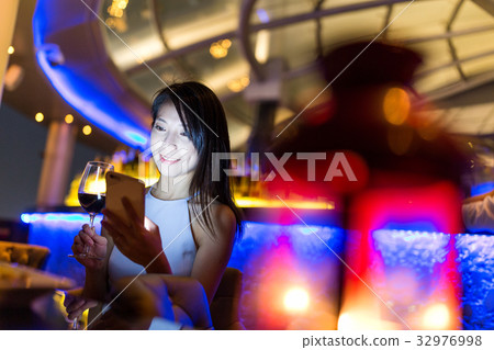 Woman use of mobile phone and enjoy her wine at sky bar 32976998