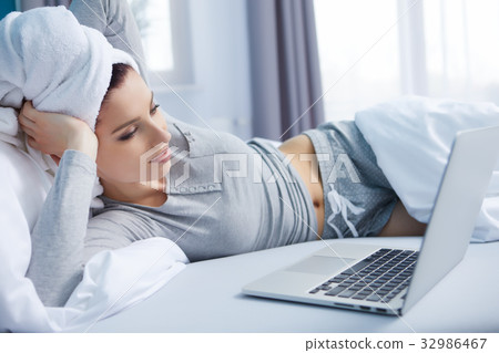 smiley young woman lying in her bed with laptop 32986467