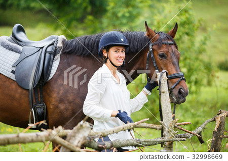 Young rider woman in helmet holding bay horse Young rider woman in helmet holding bay horse 32998669