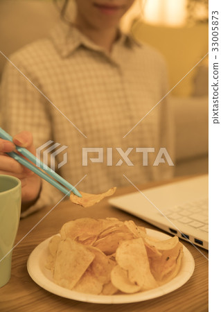 Woman eating potato chips with tongs at night while working on a computer 33005873
