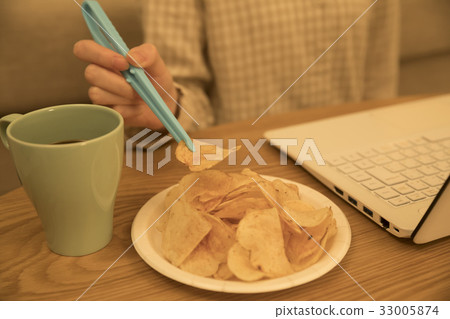 Woman eating potato chips with tongs at night while working on a computer 33005874