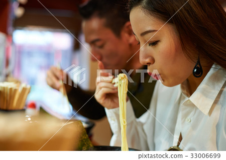 A woman is blowing on ramen at a restaurant. 33006699