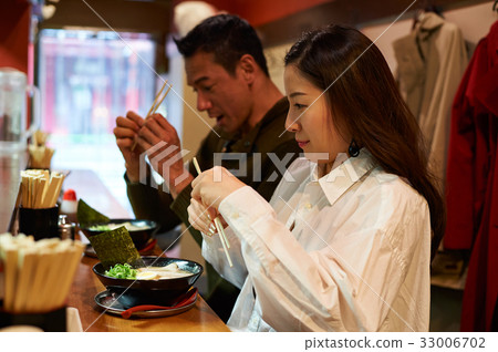 A couple is holding their chopsticks and looking at food. A couple is holding their chopsticks and looking at food. 33006702