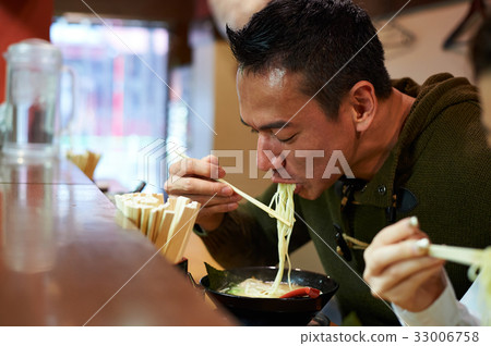 the man is eating noodles in the restaurant 33006758