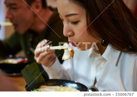 a girl is eating and picking up slice of meat by chopsticks 33006767