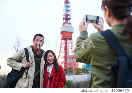 a girl is taking photo of couple near a tower 33006779