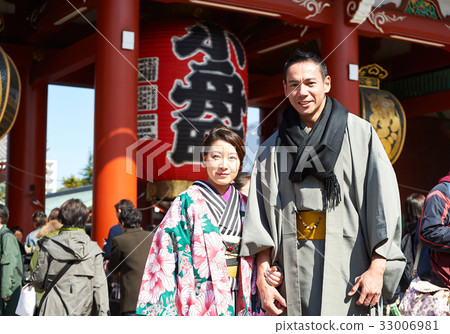 A young couple in kimono is standing in front of the temple and smiling. 33006981